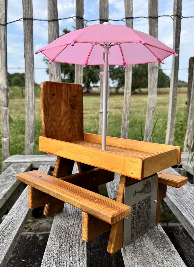 Houten picknicktafeltje met roze parasol en een gegraveerd plaatje met logo en QR-code